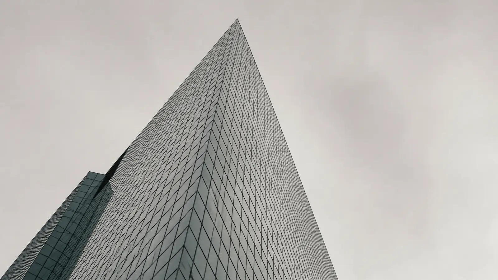 Die Glasfassade eines Bankturms von unten gegen einen flachen grauen Himmel