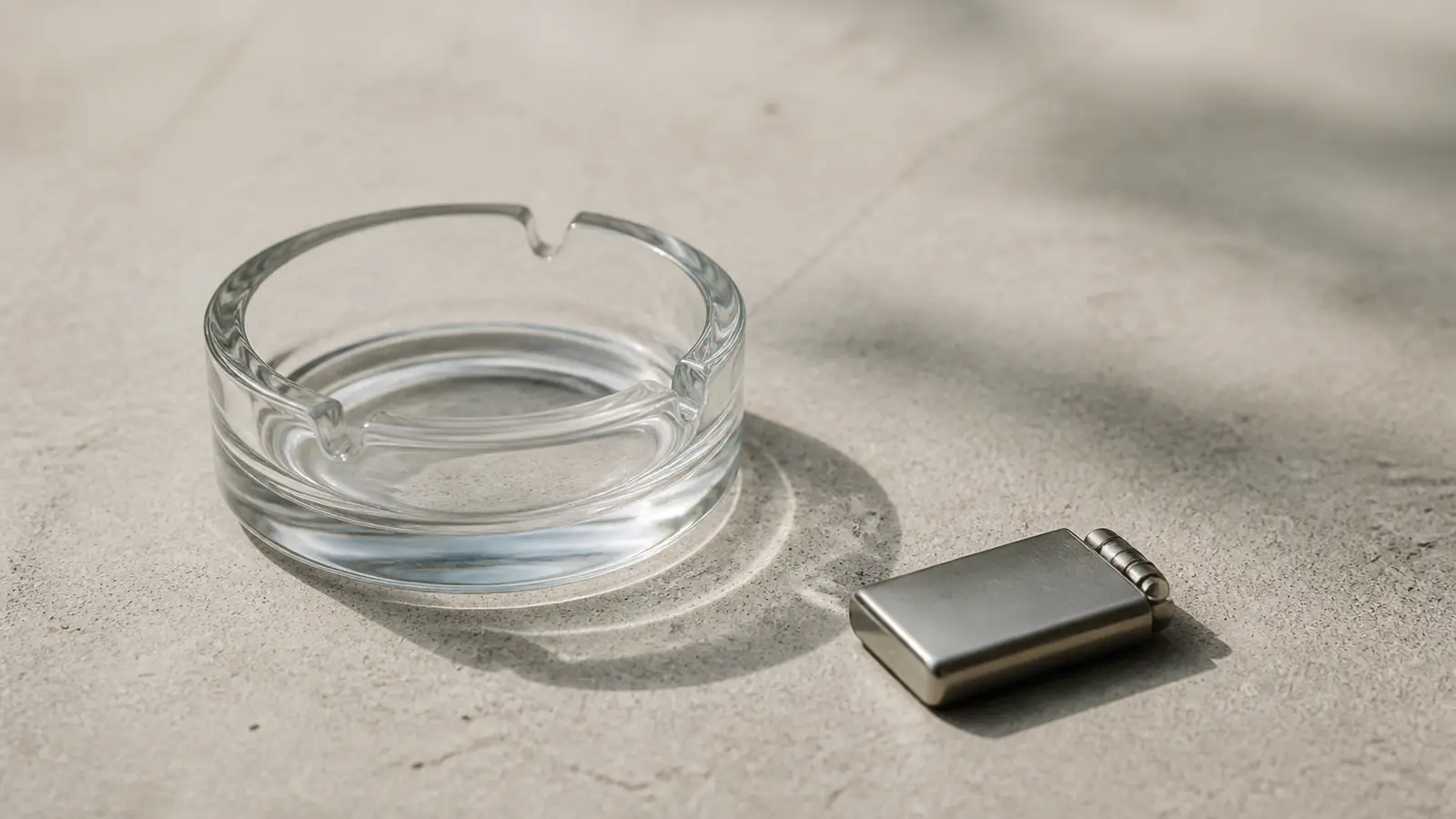 Ein leerer Glasaschenbecher und ein kleines Metallgerät auf einer hellen Betonfläche
