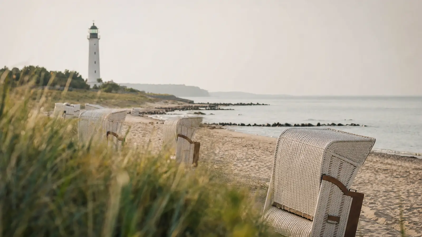 Ostseestrand mit wei&szlig;em Leuchtturm in der Ferne und leeren Strandk&ouml;rben